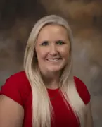 Portrait of a smiling woman with long blonde hair wearing a red top, posed against a neutral studio backdrop.