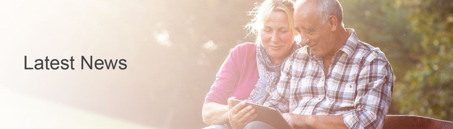 Middle age couple sitting on park bench checking news on iPad