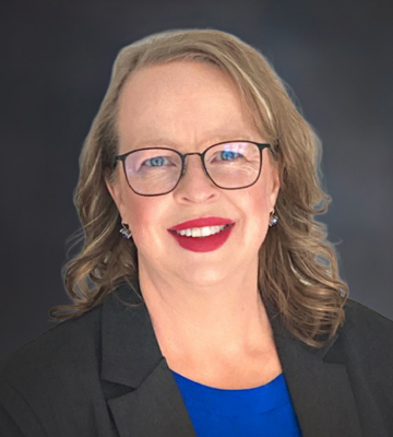 Professional headshot of a smiling woman with glasses, wearing a blue top and black blazer against a dark gradient background.