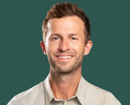 Smiling man with short brown hair wearing a light button-down shirt, head-and-shoulders portrait on a teal background.