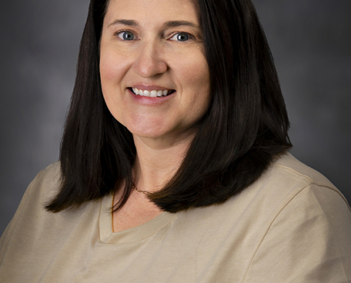 Portrait of a smiling woman with shoulder-length dark hair wearing a beige shirt with Jefferson Community Health & Life logo.
