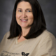 Portrait of a smiling woman with shoulder-length dark hair wearing a beige shirt with Jefferson Community Health & Life logo.