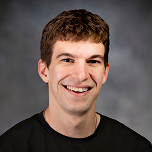 Portrait of a smiling man with short brown hair wearing a black shirt, looking at the camera.
