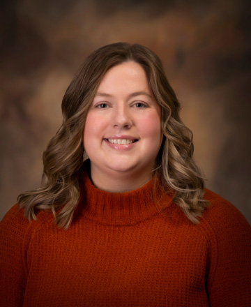 Portrait of a smiling woman with wavy light brown hair wearing an orange knit sweater against a warm brown studio backdrop